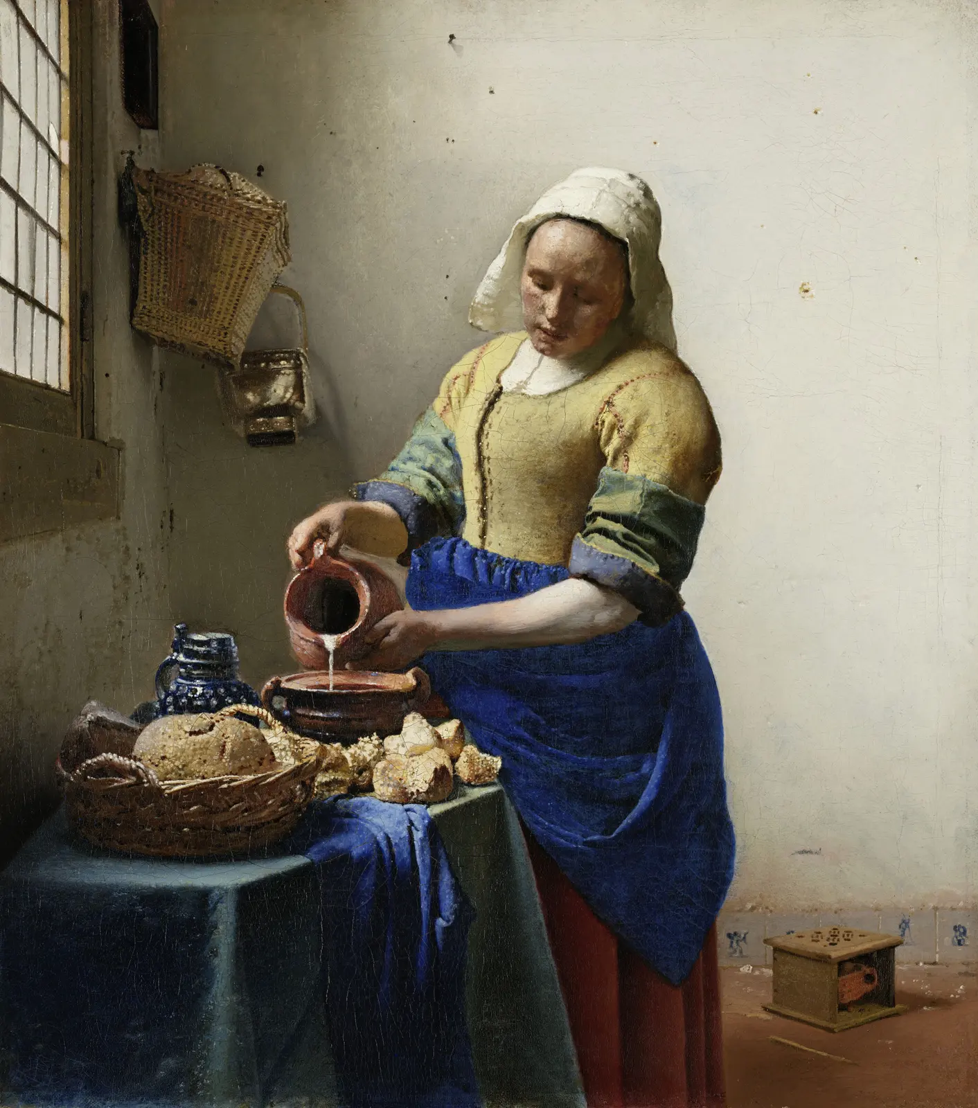 A maid in a yellow bodice and blue apron pours milk from a jug at a table with bread, beside a window on the left wall.